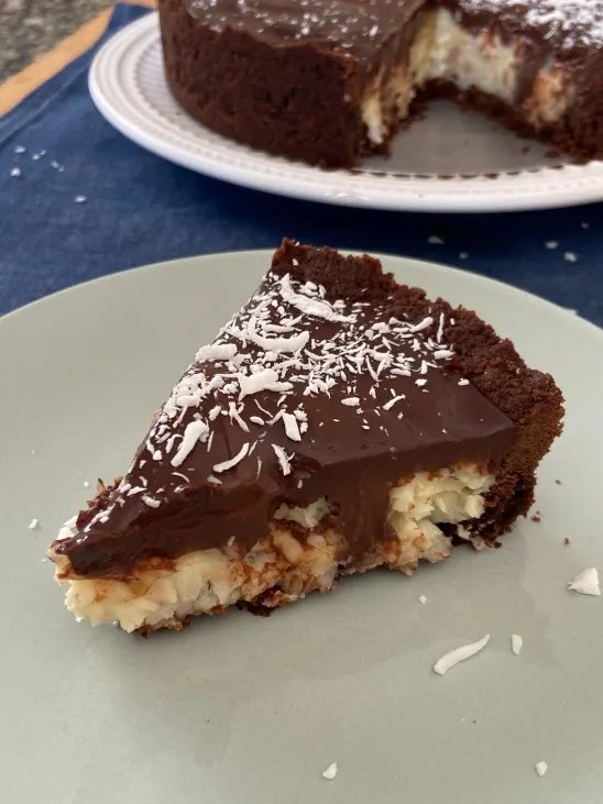 Fatia de torta de prestígio com recheio de coco, cobertura de chocolate e coco ralado